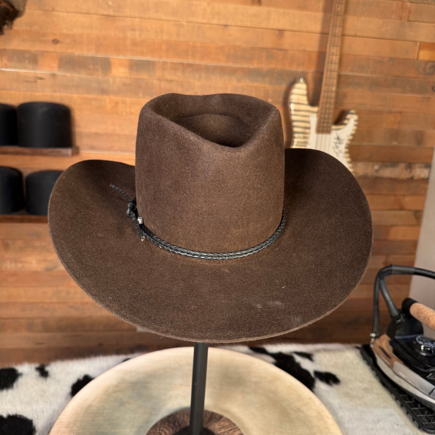 Brown cowboy hat on a stand with a guitar and cowhide rug in the background