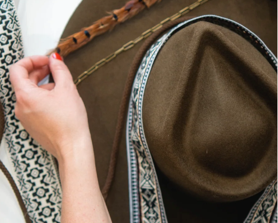 Brown hat with decorative band held by a person against a patterned background