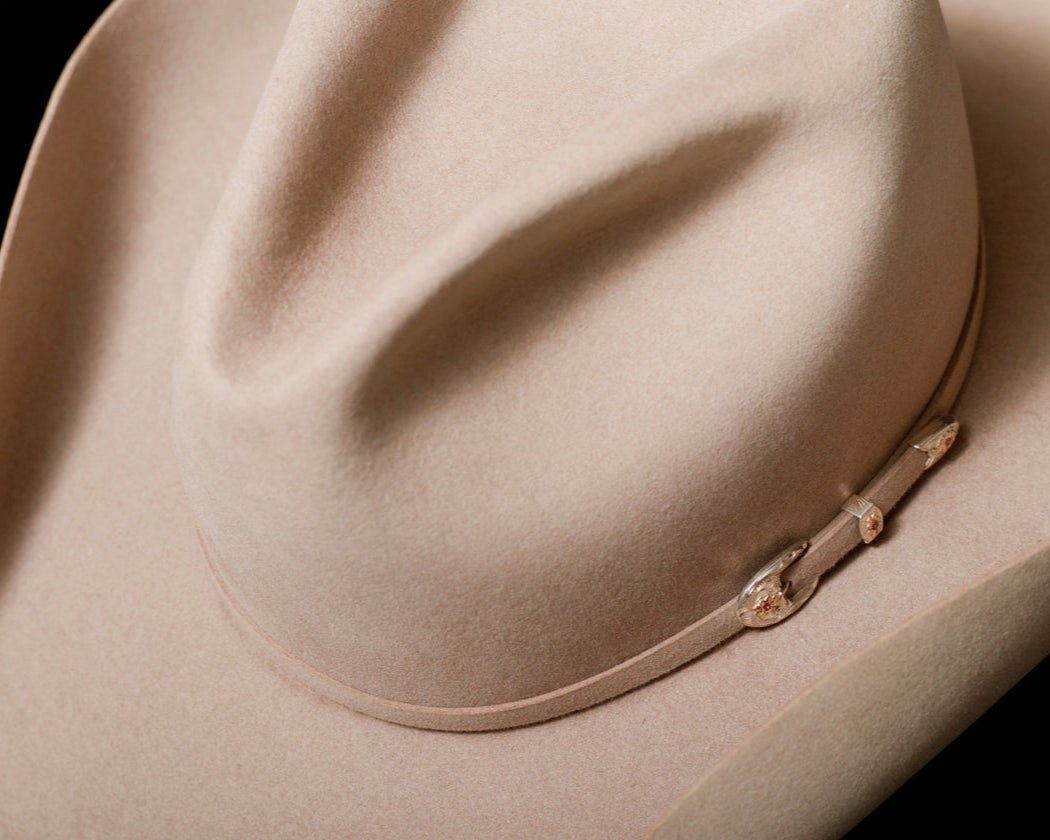 Close-up of a beige cowboy hat with a band on a black background