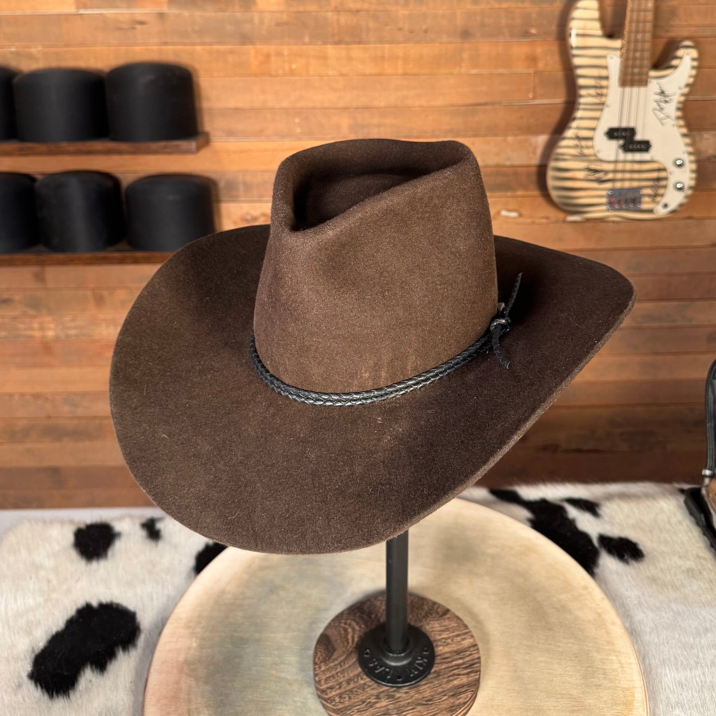 Brown cowboy hat hanging on a wooden wall with musical instruments in the background